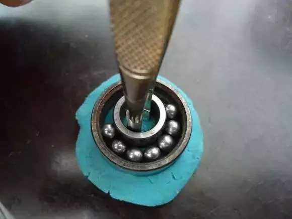 用鑷子或別的相近的物體越過內(nèi)圈，同時向滾珠的方向用力頂住